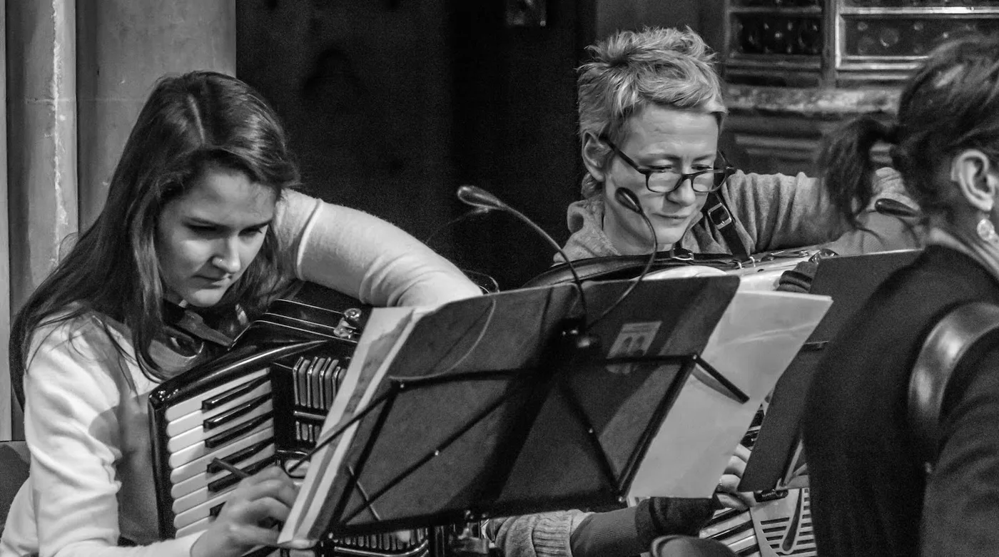 Black and white photograph of two accordion players reading from music stands during a rehearsal