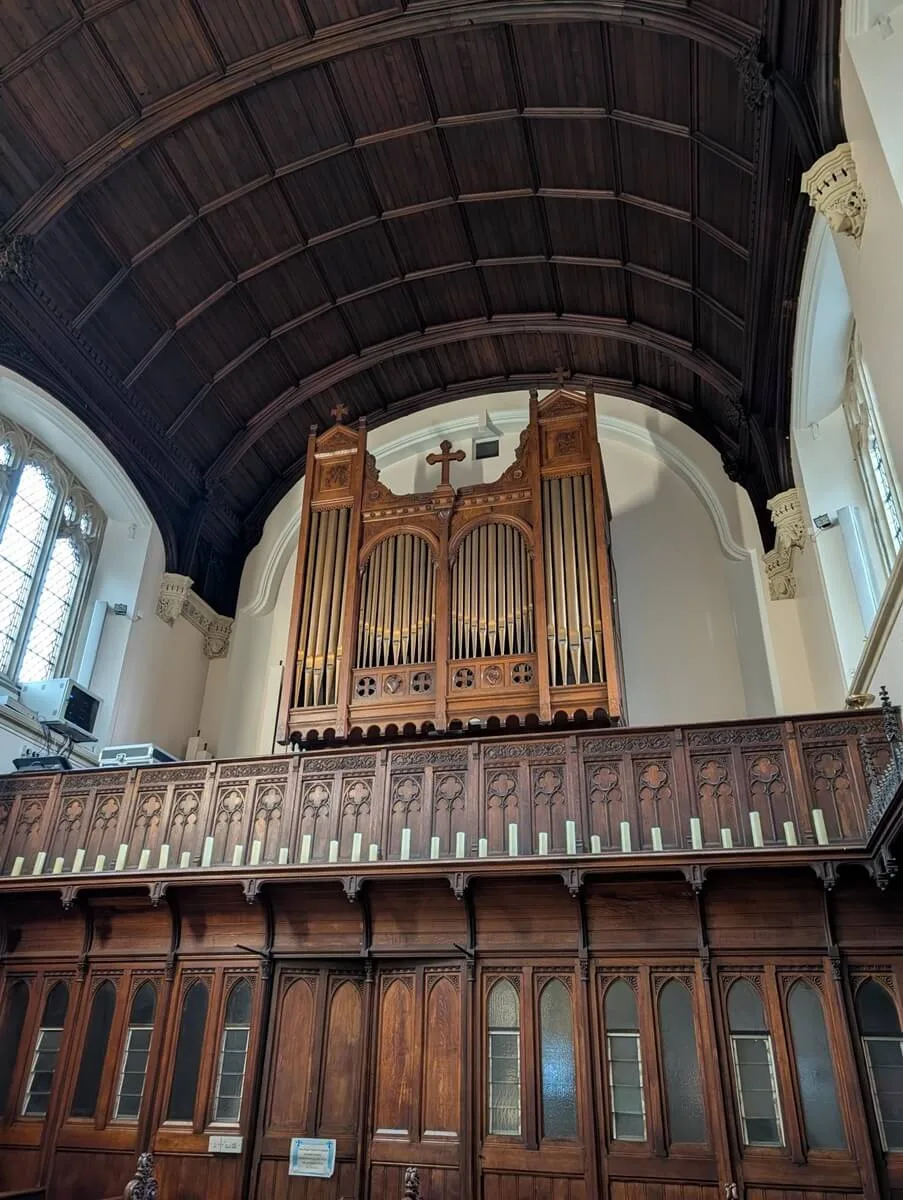 The Loret organ's carved wooden case with silver pipes, set in a gallery above carved oak panelling under the chapel's dark timber barrel roof