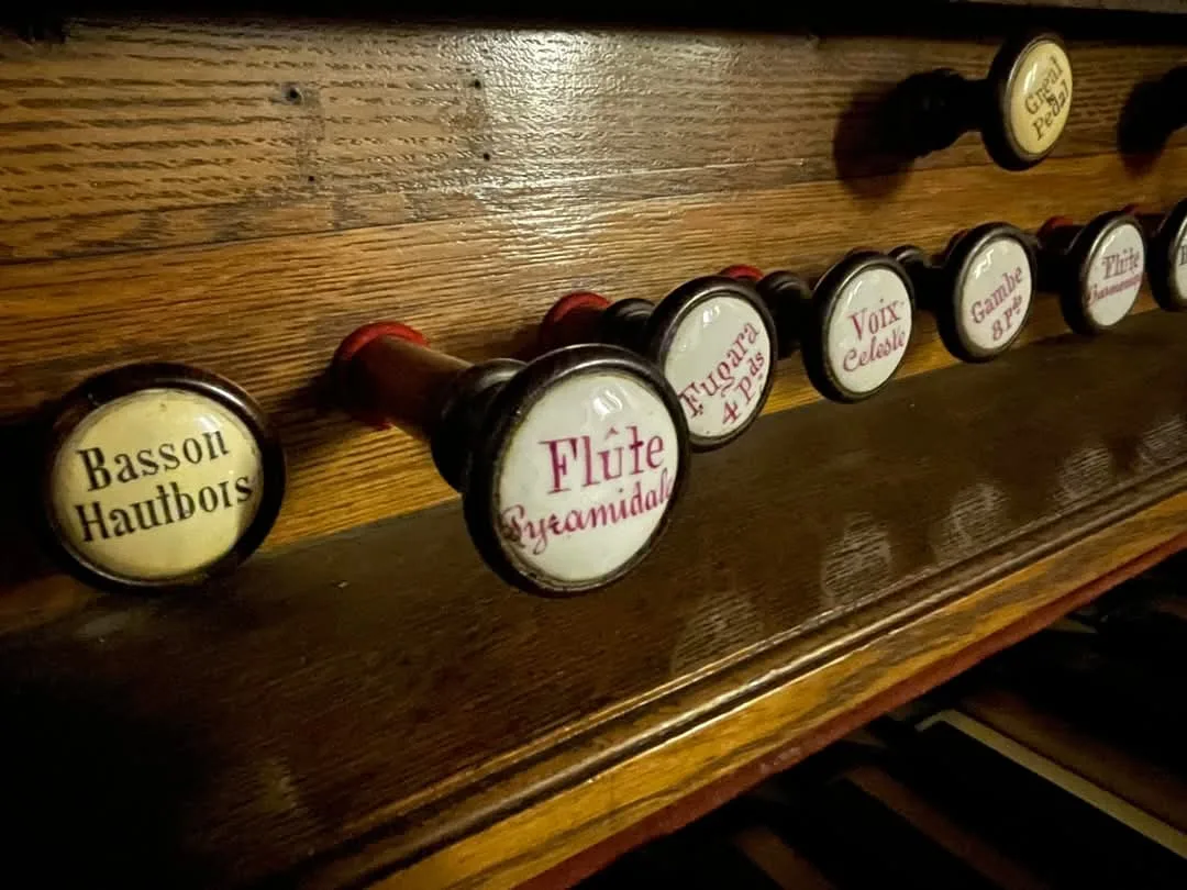 Close-up of white porcelain organ stop knobs with French names in red and black script, including Basson Hautbois, Flûte Pyramidale, Fugara 4 pieds, Voix Céleste and Gambe 8 pieds